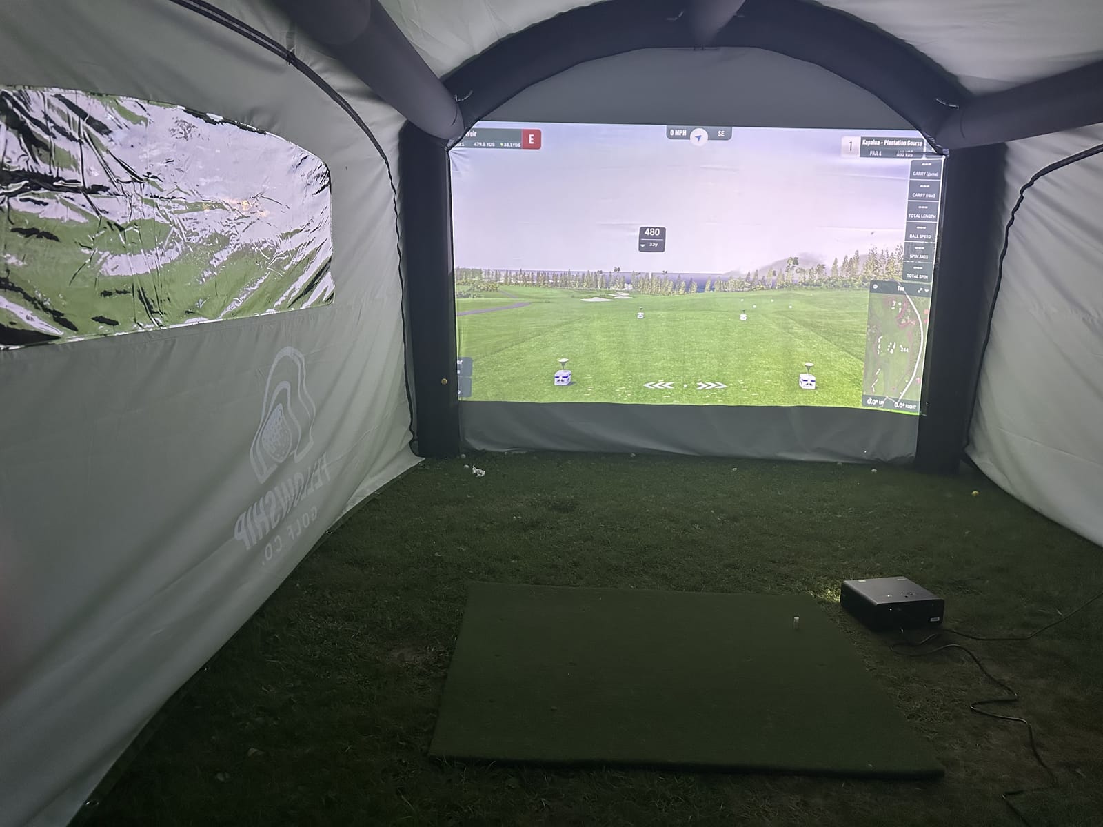 Interior of the simulator tent — hitting mat, screen, and clubs